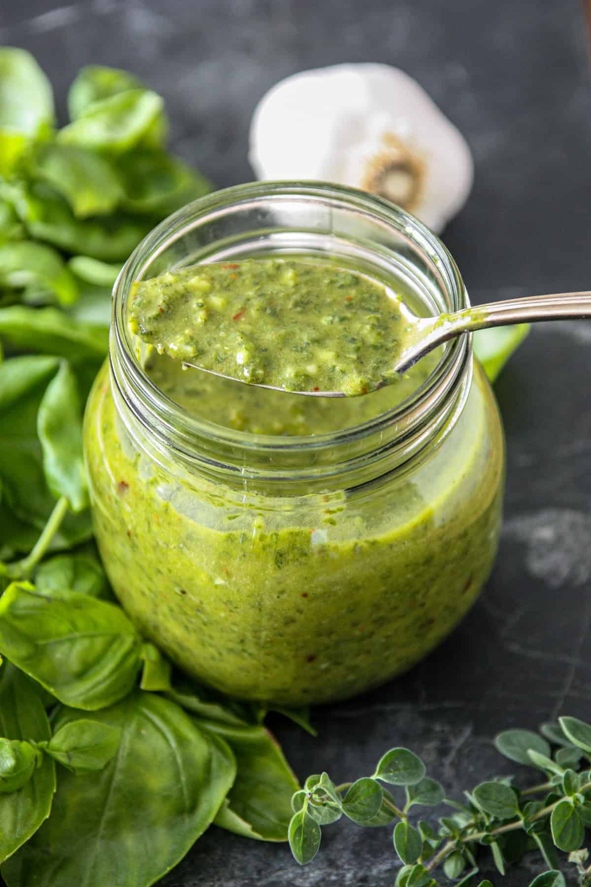 A spoon dipped into a jar of basil chimichurri sauce.