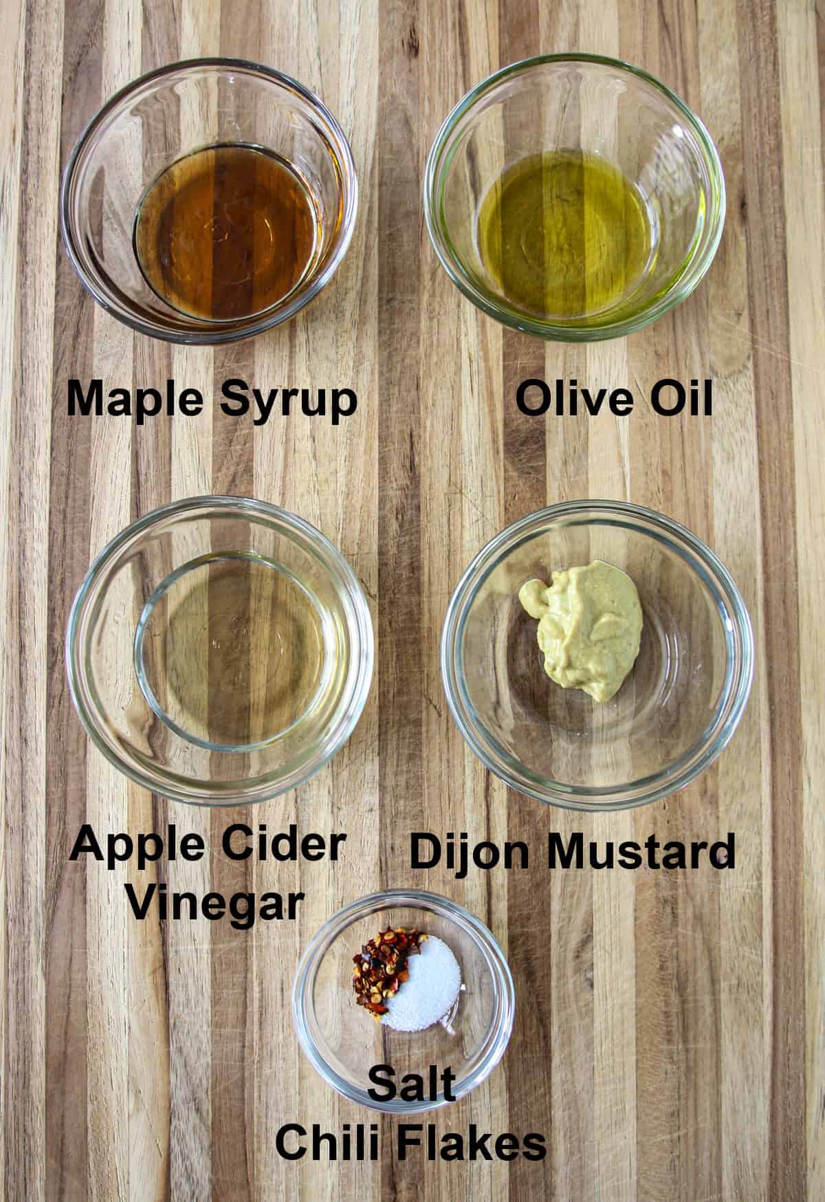 The ingredients for making the vinaigrette in glass dishes on a wooden board.